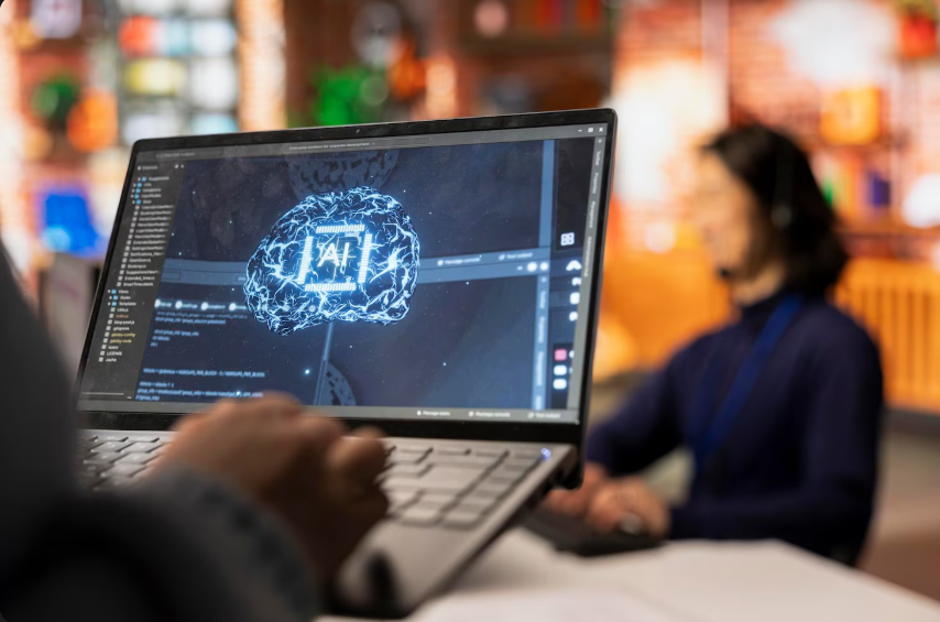 Person using a laptop displaying an AI brain interface and coding software during a tech workspace session.
